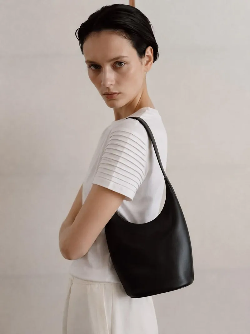 Mujer de cabello corto con camiseta blanca de mangas plisadas y bolso negro de cuero al hombro